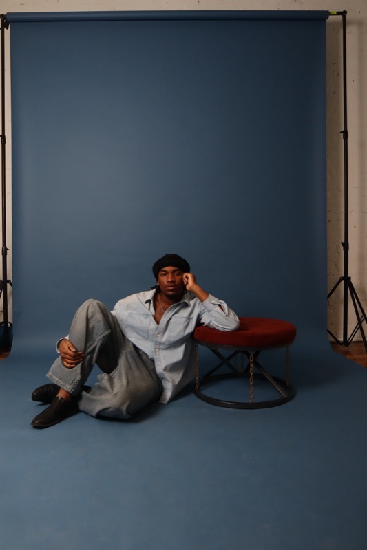 Osa Deraé sitting on the floor of a blue photo studio